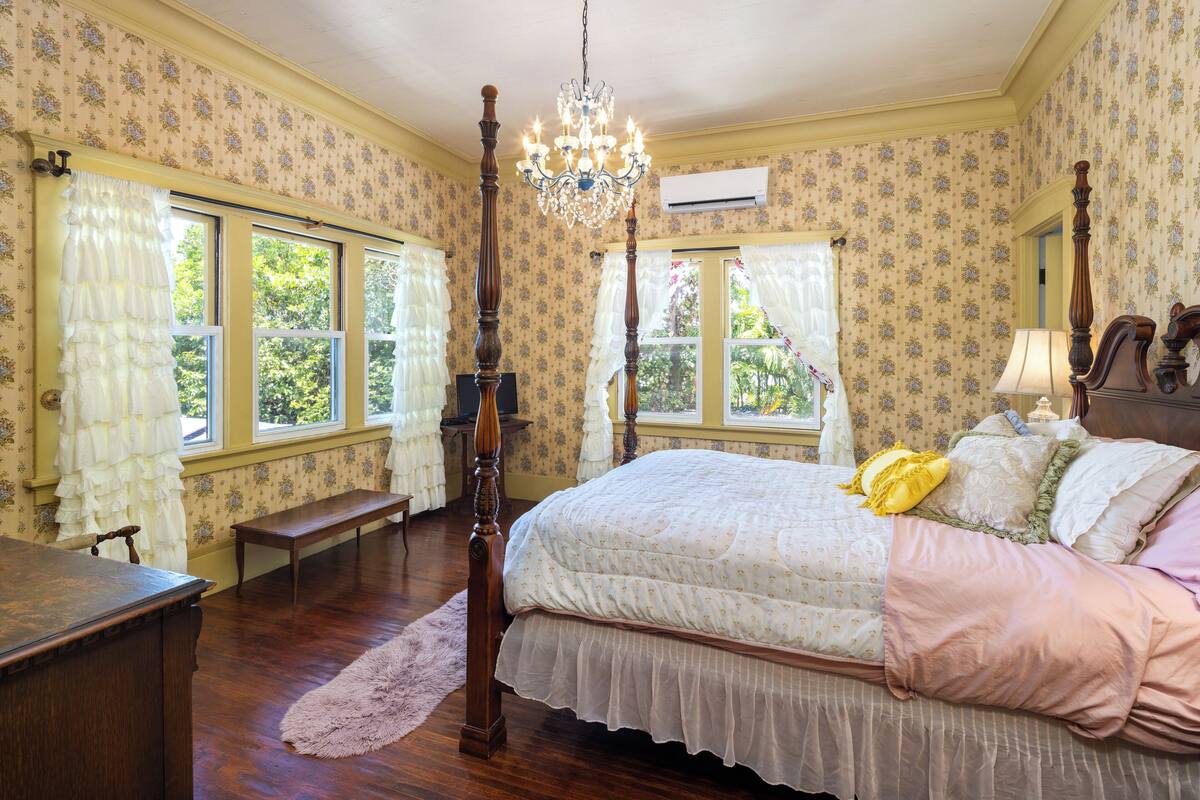 Une chambre à coucher avec un lit à baldaquin, un lustre et un papier peint à motifs floraux.