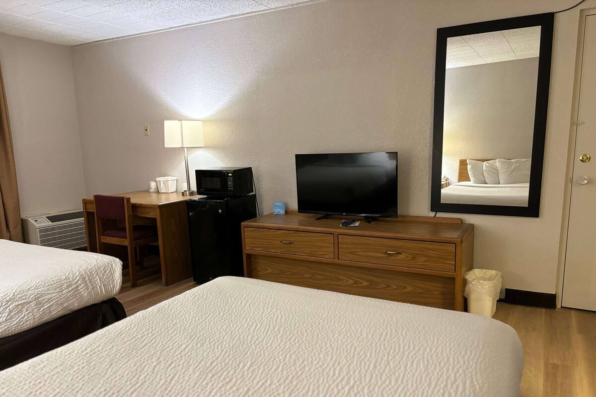 A hotel room with two beds, a desk with a computer, a television, a microwave, and a mirror.