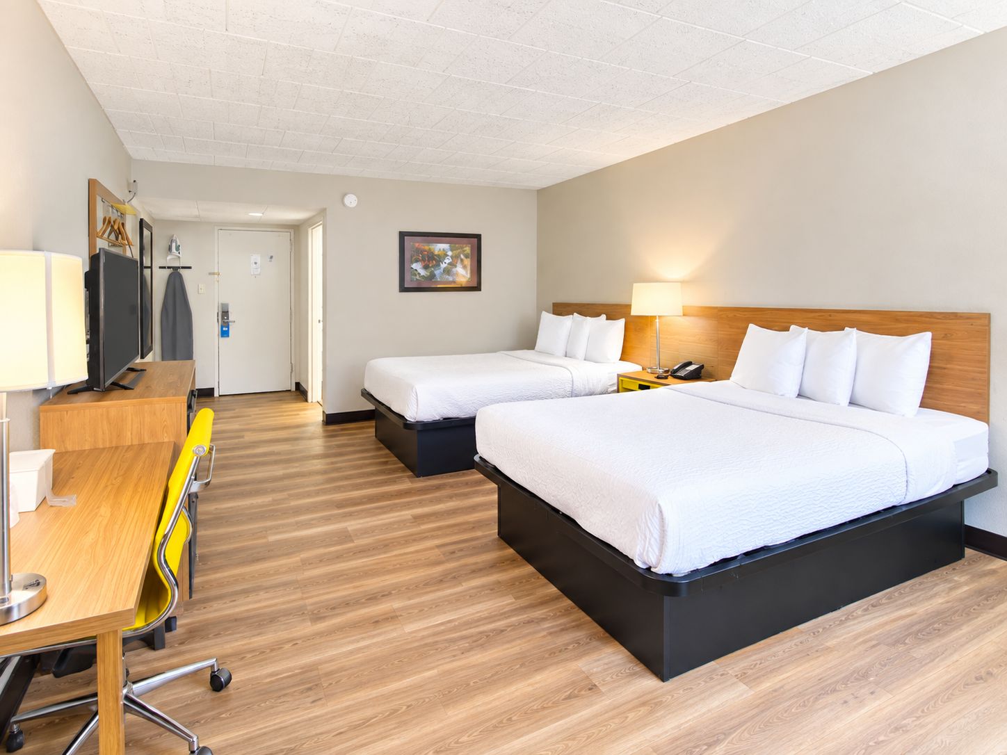 A hotel room with two beds, a desk with a chair, a television, and a painting on the wall.
