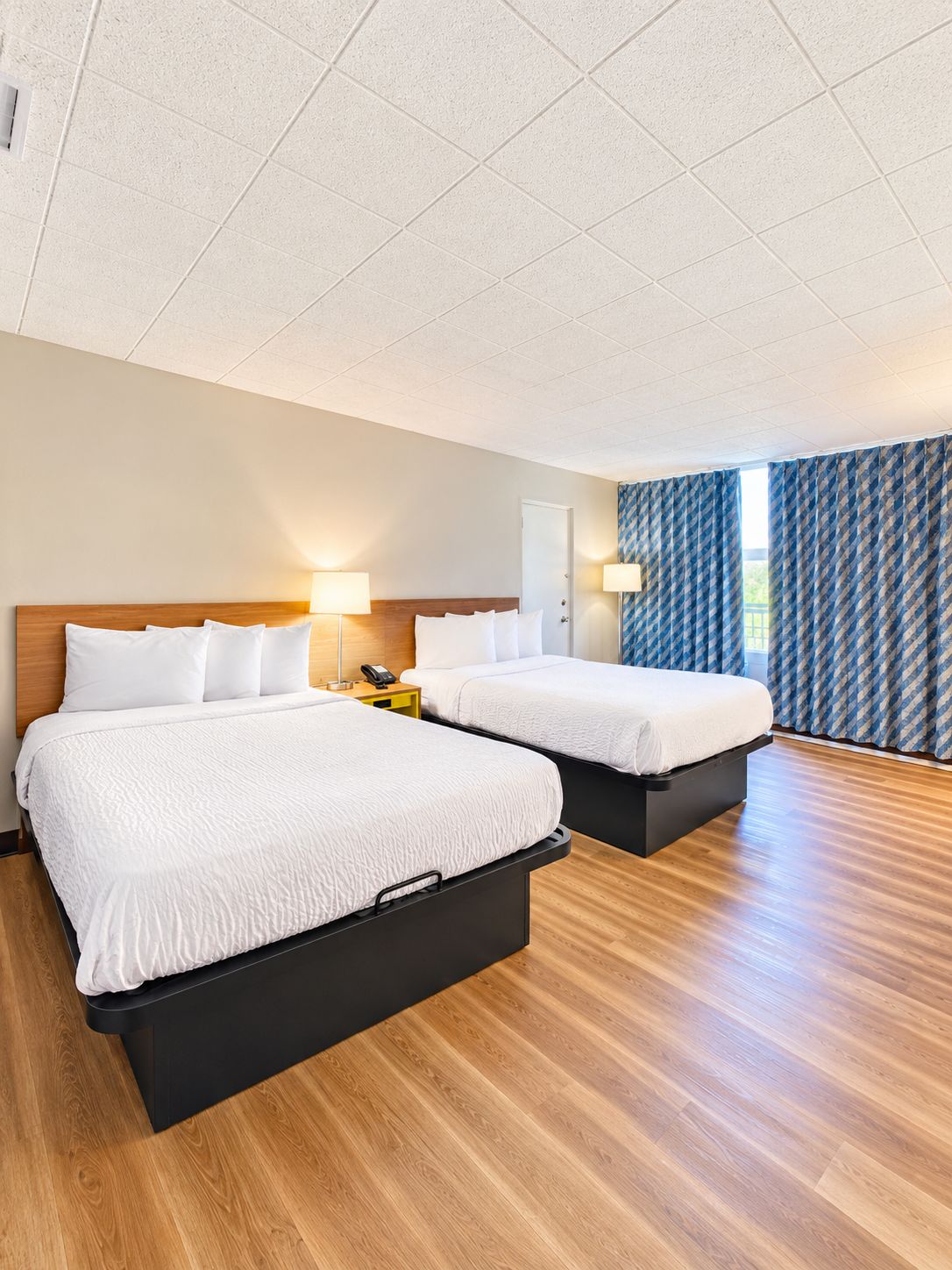 A hotel room with two beds, a wooden floor, and a view of the outdoors.