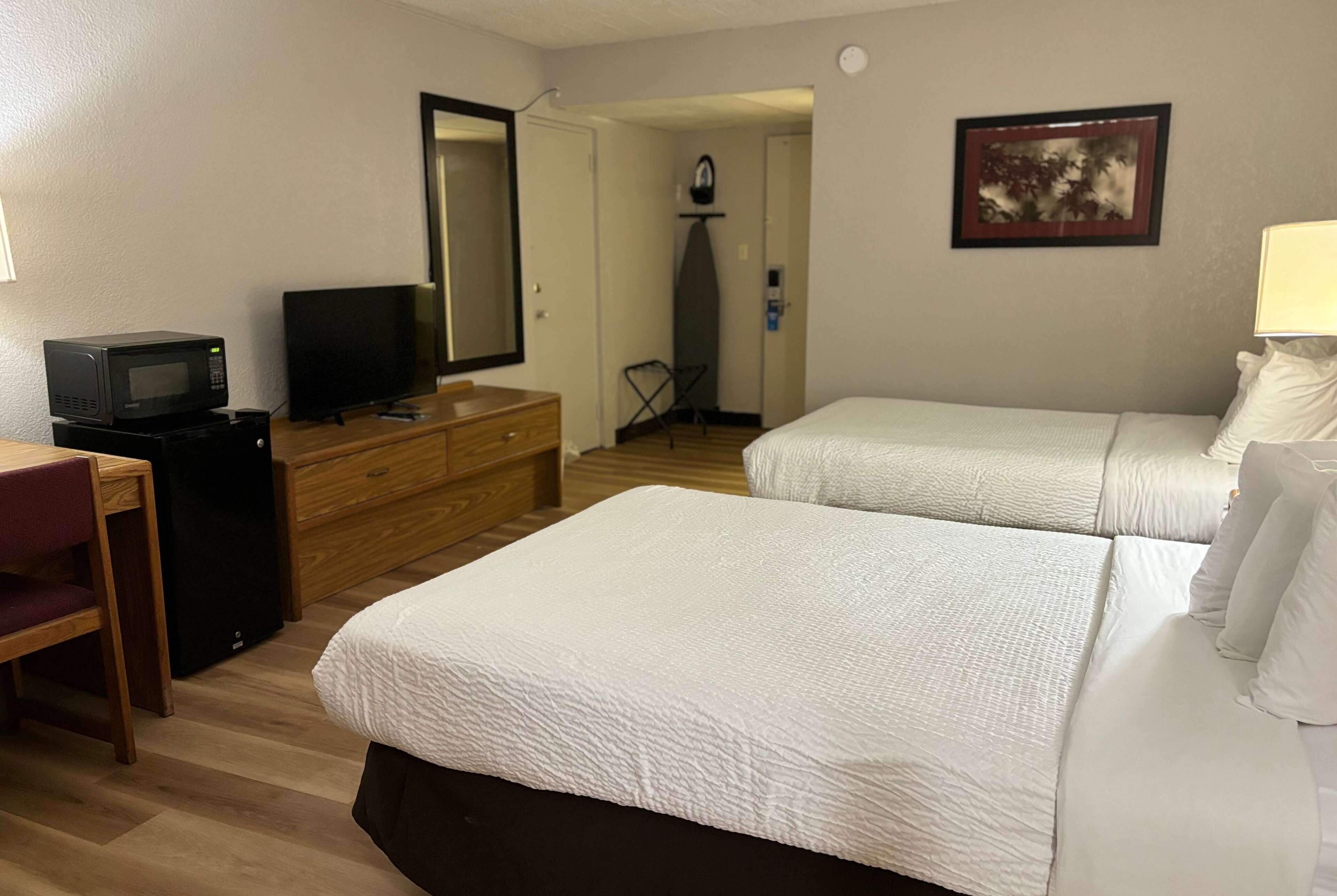 Habitación de hotel con dos camas, televisión, microondas y cómoda.