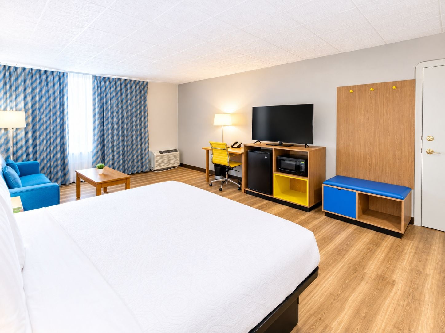 A hotel room with a bed, a desk with a computer, a television, and a wardrobe.