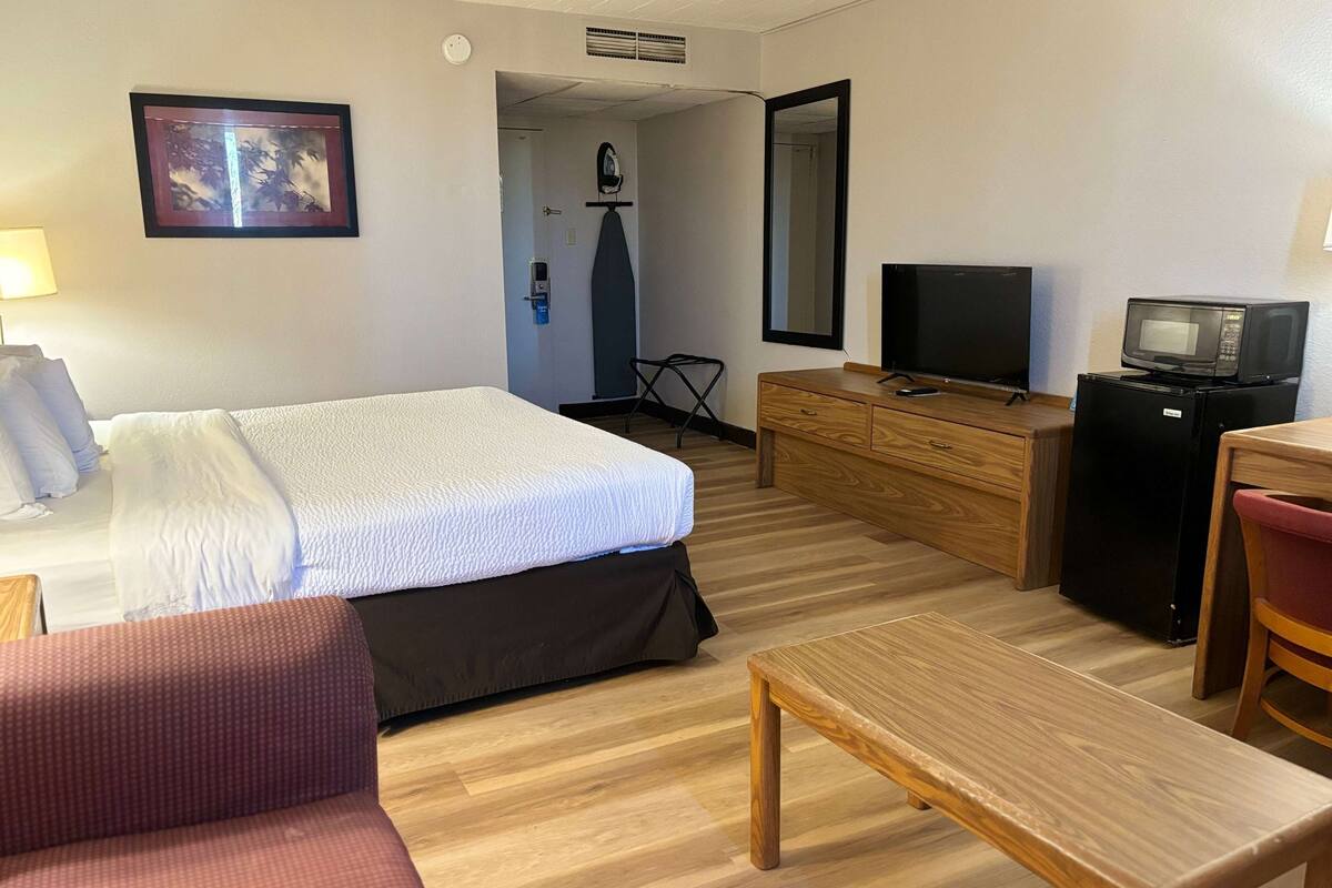 A hotel room with a bed, a wooden dresser, a television, a microwave, a desk, and a chair.