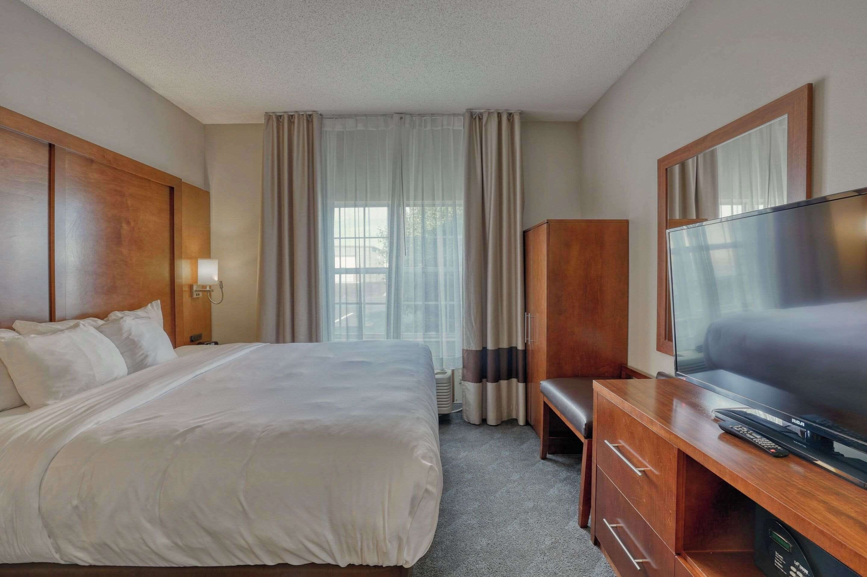 Una habitación de hotel con una cama grande, un escritorio de madera con televisor y un armario.