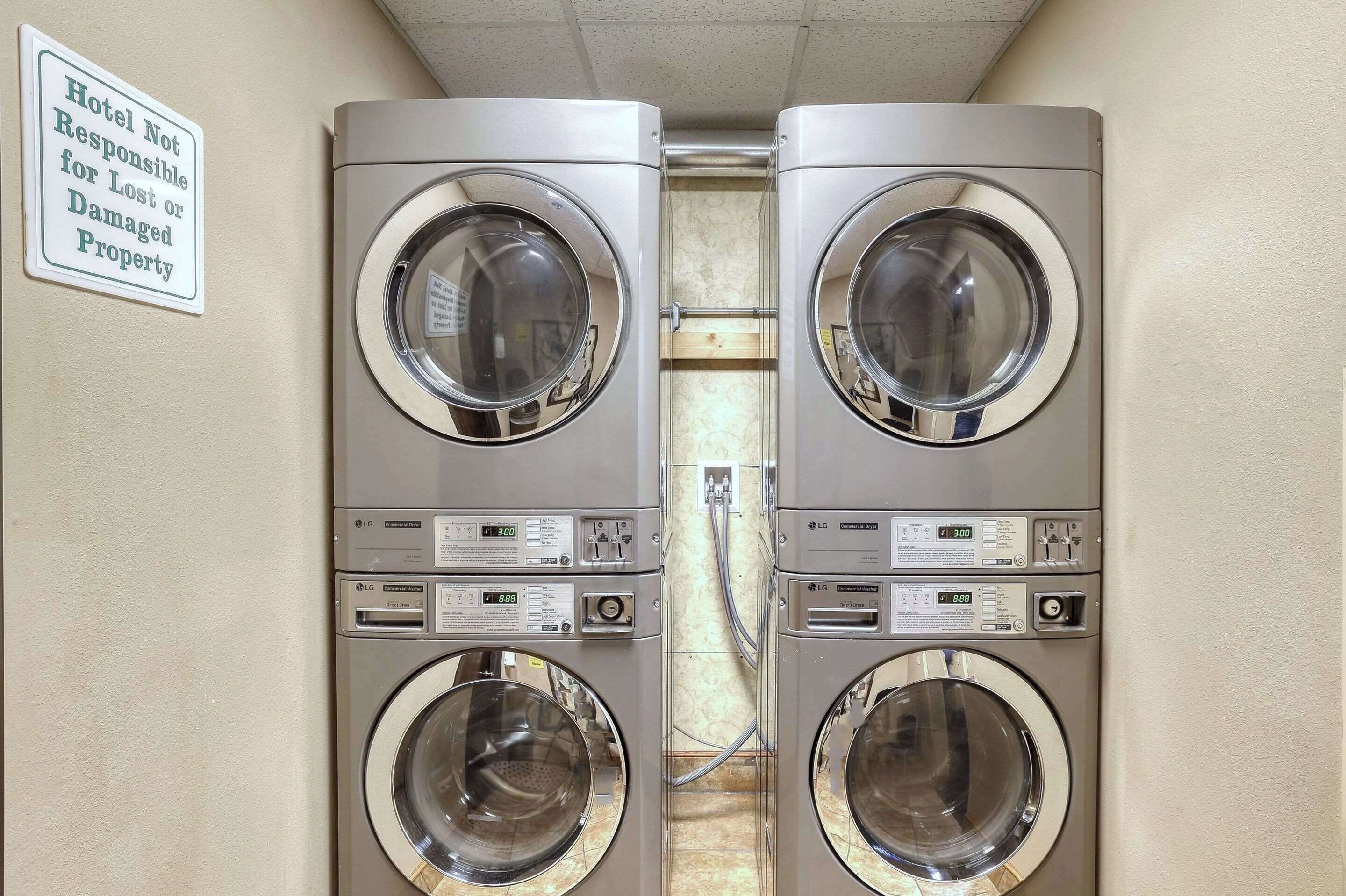 Une buanderie équipée de deux machines à laver LG à chargement frontal, avec un panneau indiquant : « L’hôtel n’est pas responsable des objets perdus ou endommagés. »