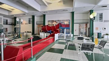 Amplio espacio interior con un tobogán rojo, suelo a cuadros y un comedor con mesas y sillas.