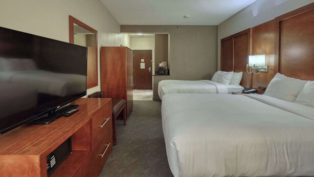A hotel room with a TV, two beds, a wooden wardrobe, and a mirror. - Comfort Suites Appleton Airport (Appleton)