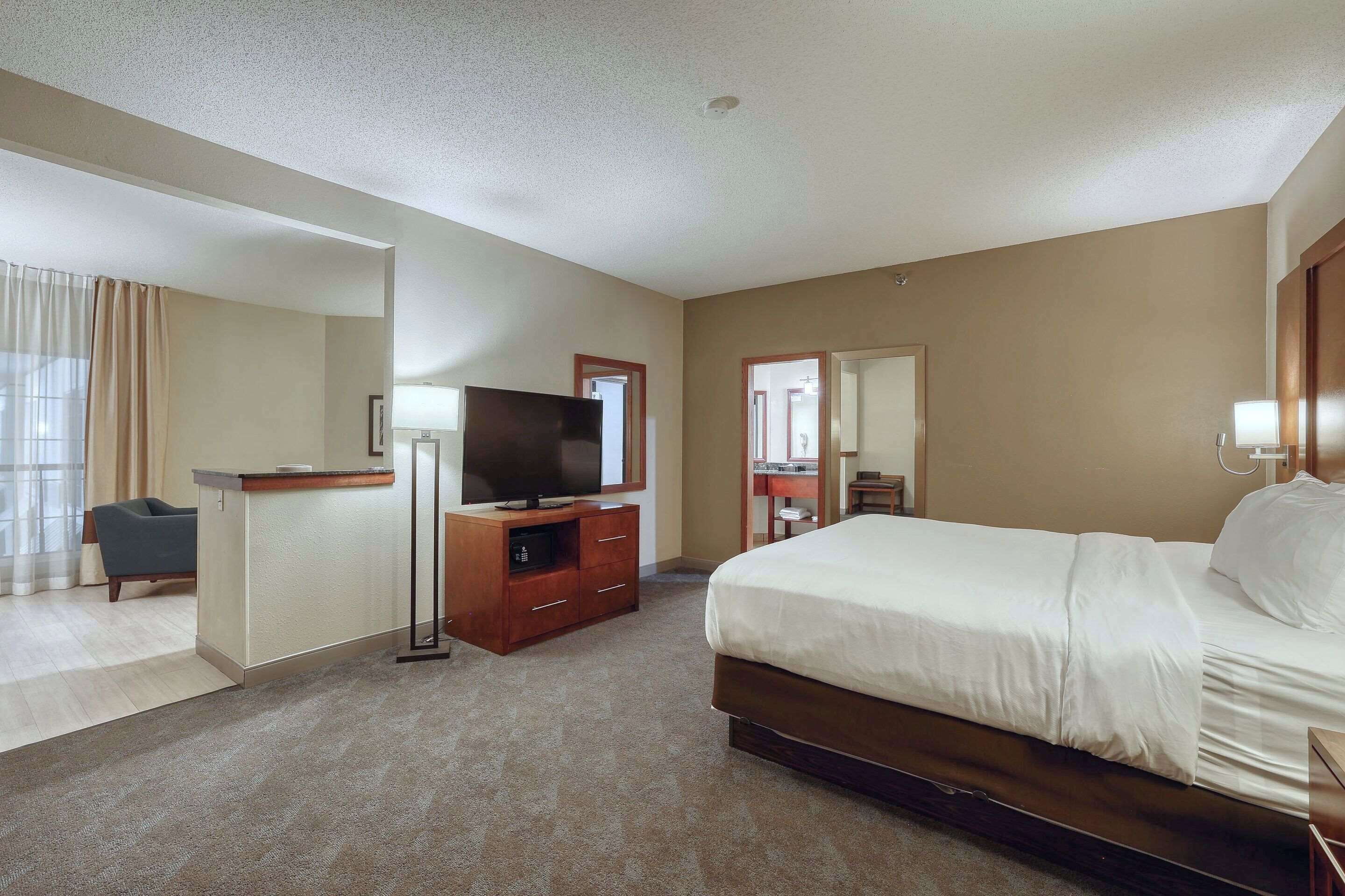 A hotel room with a large bed, a desk with a flat-screen TV, a chair, and a mirror.