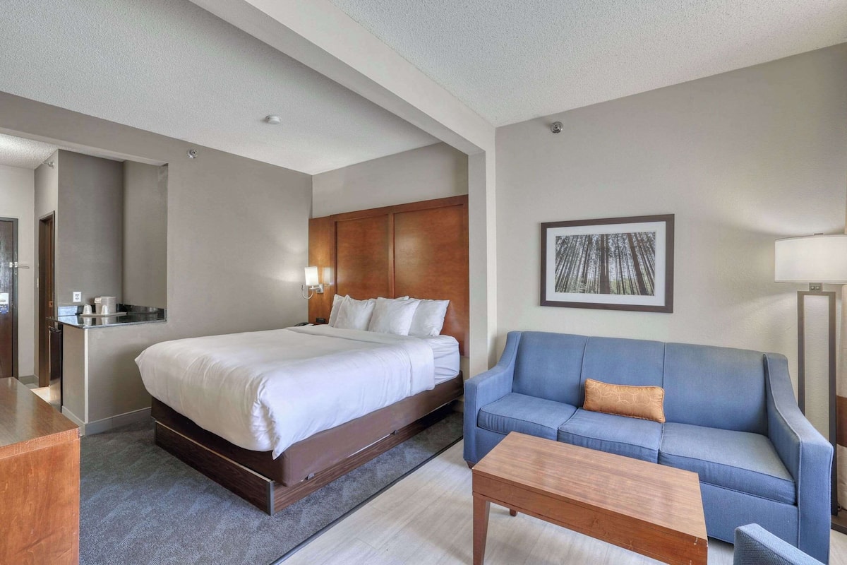 A hotel room with a large bed, a blue sofa, a wooden coffee table, and a framed picture on the wall.