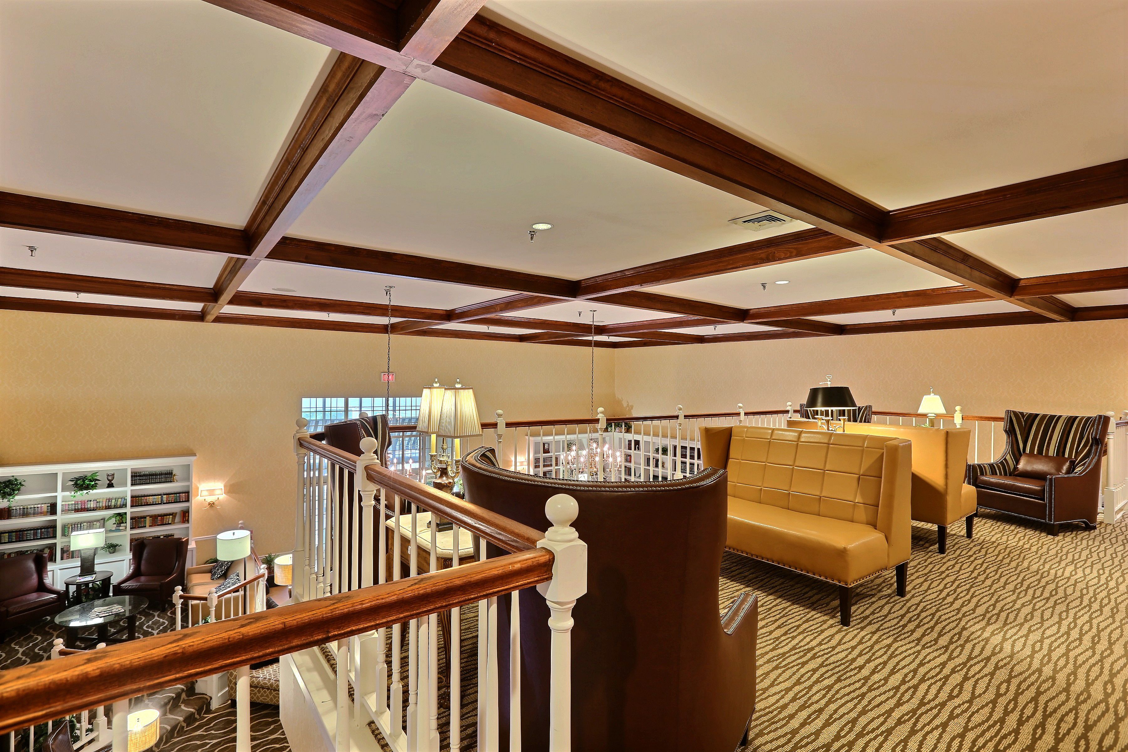 Un hall de hotel espacioso con techo alto, vigas de madera, una escalera, una zona de estar con sofá y sillones, y una estantería.