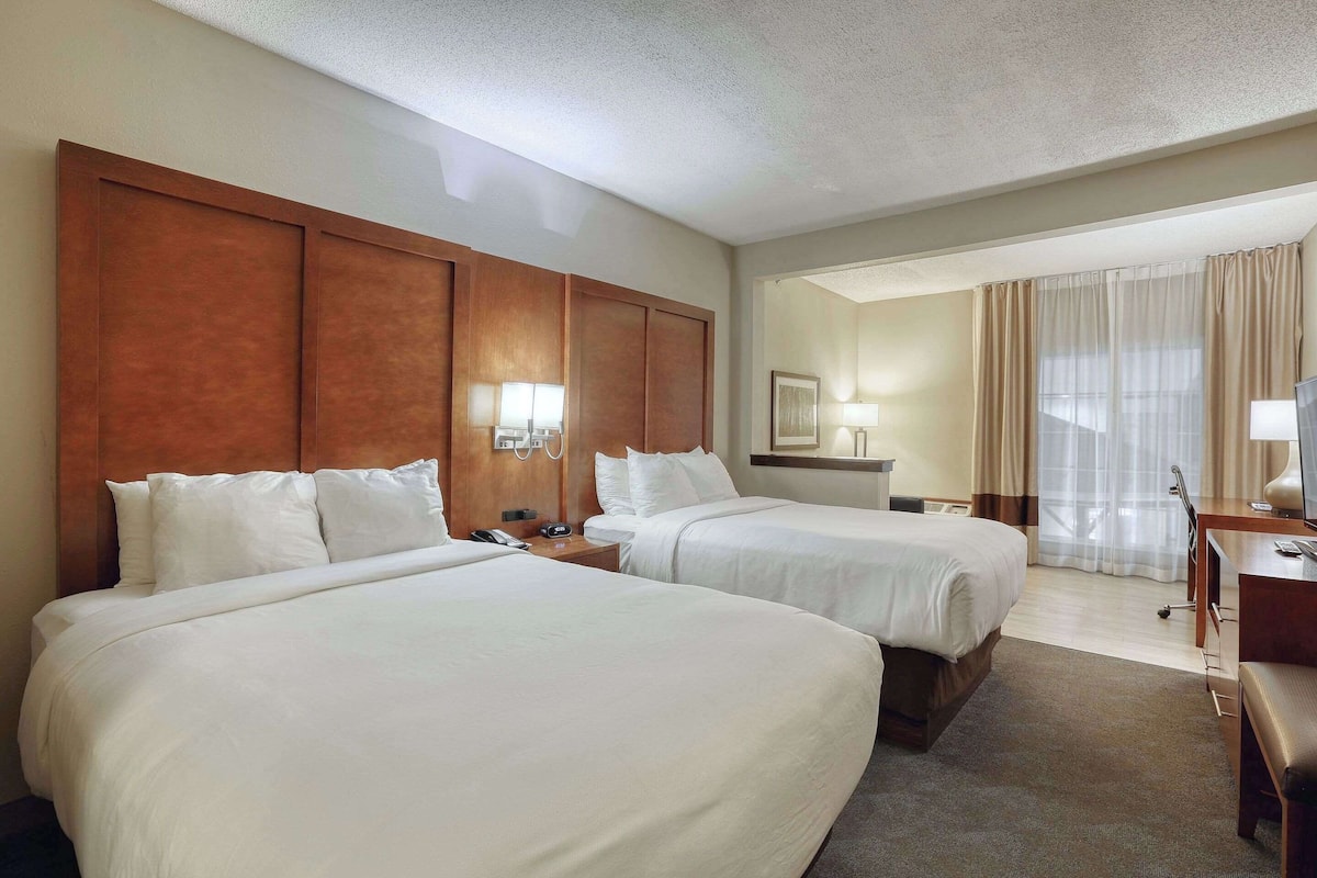 A hotel room with two beds, a desk, a chair, and a window with curtains.