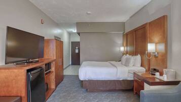 Una habitación de hotel con cama, escritorio, televisión y mini refrigerador.