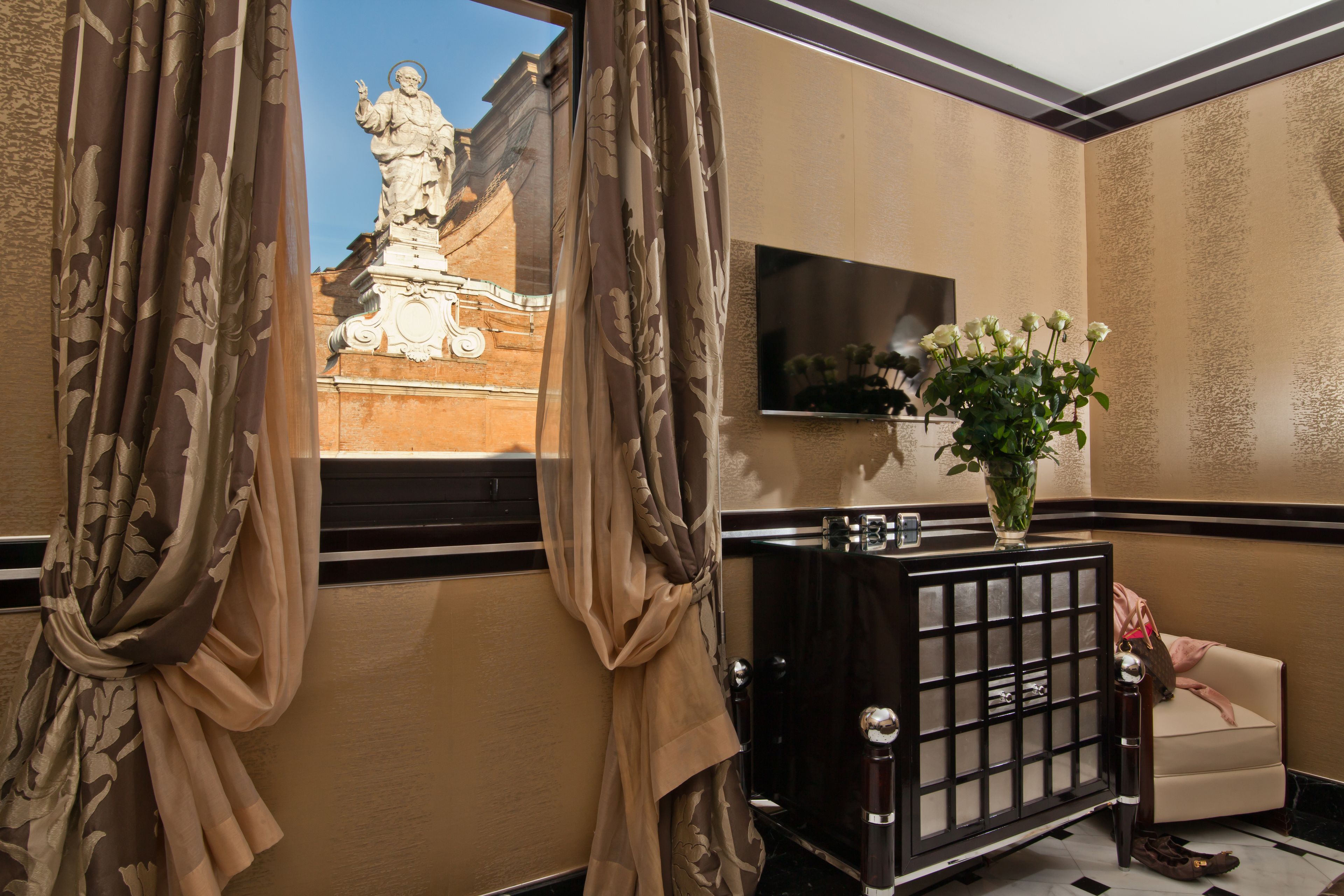 A hotel lobby with a statue, a TV, a vase with flowers, and a sofa.