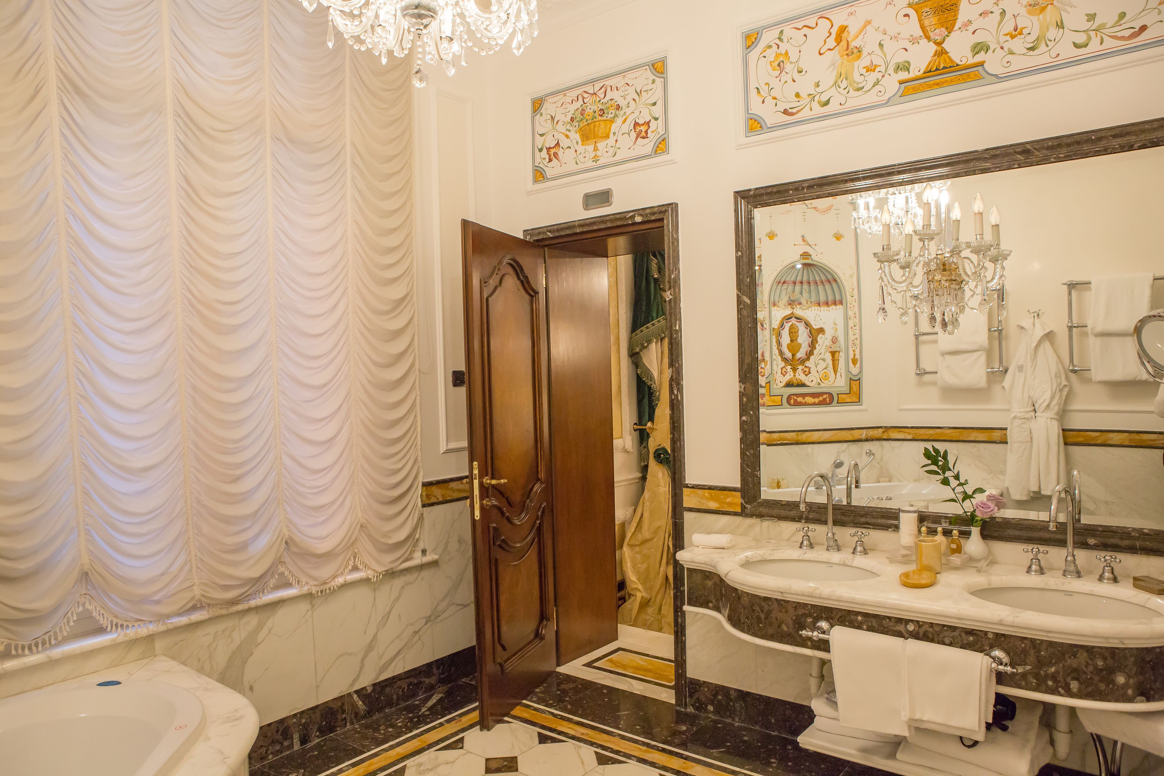 A luxurious bathroom with a large mirror, two sinks, a bathtub, and a chandelier.