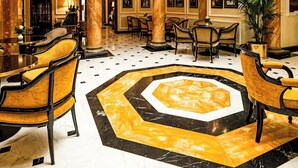A lobby with a geometric patterned floor, a central chandelier, and a large stained glass ceiling.