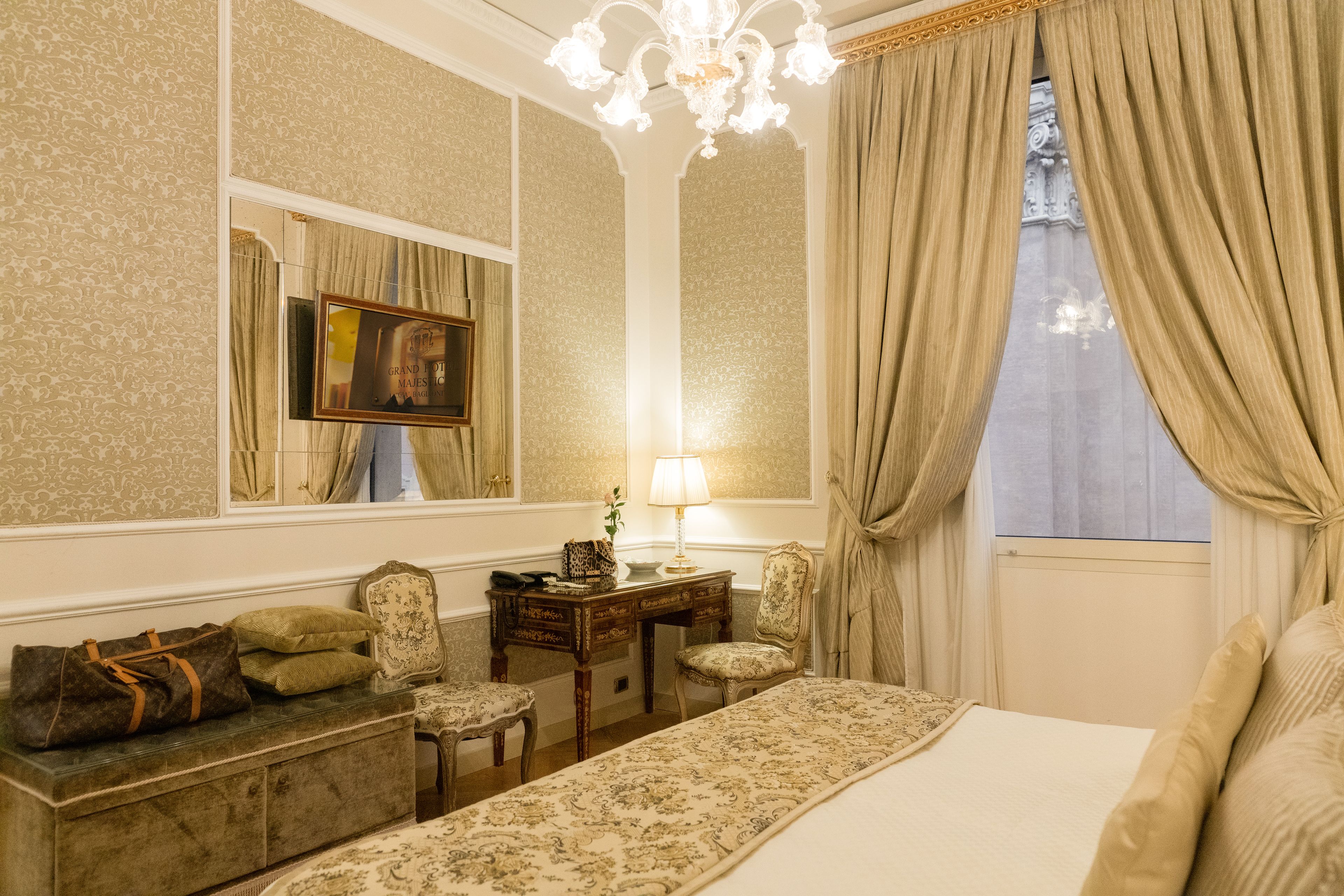A hotel room with a bed, a desk, a chair, a lamp, and a window with curtains.