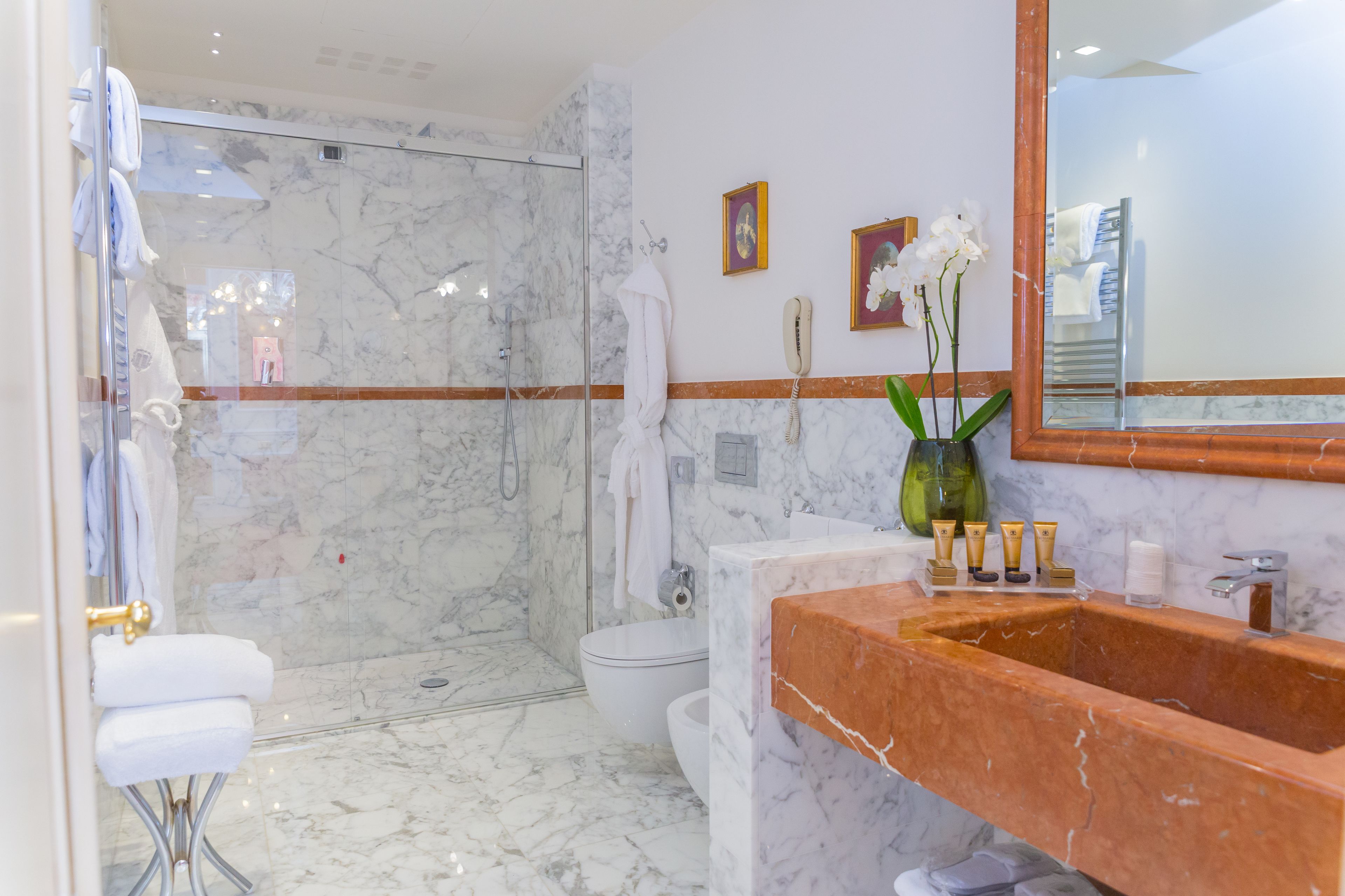A modern bathroom with a marble floor, a glass-enclosed shower, a white toilet, and a vanity with a marble sink.