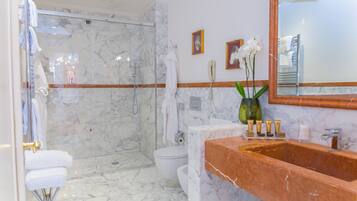 A modern bathroom with a marble floor, a glass-enclosed shower, a white toilet, and a vanity with a marble sink.