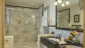 A bathroom with a glass-enclosed shower, marble walls, and a vanity with two sinks and a large mirror.