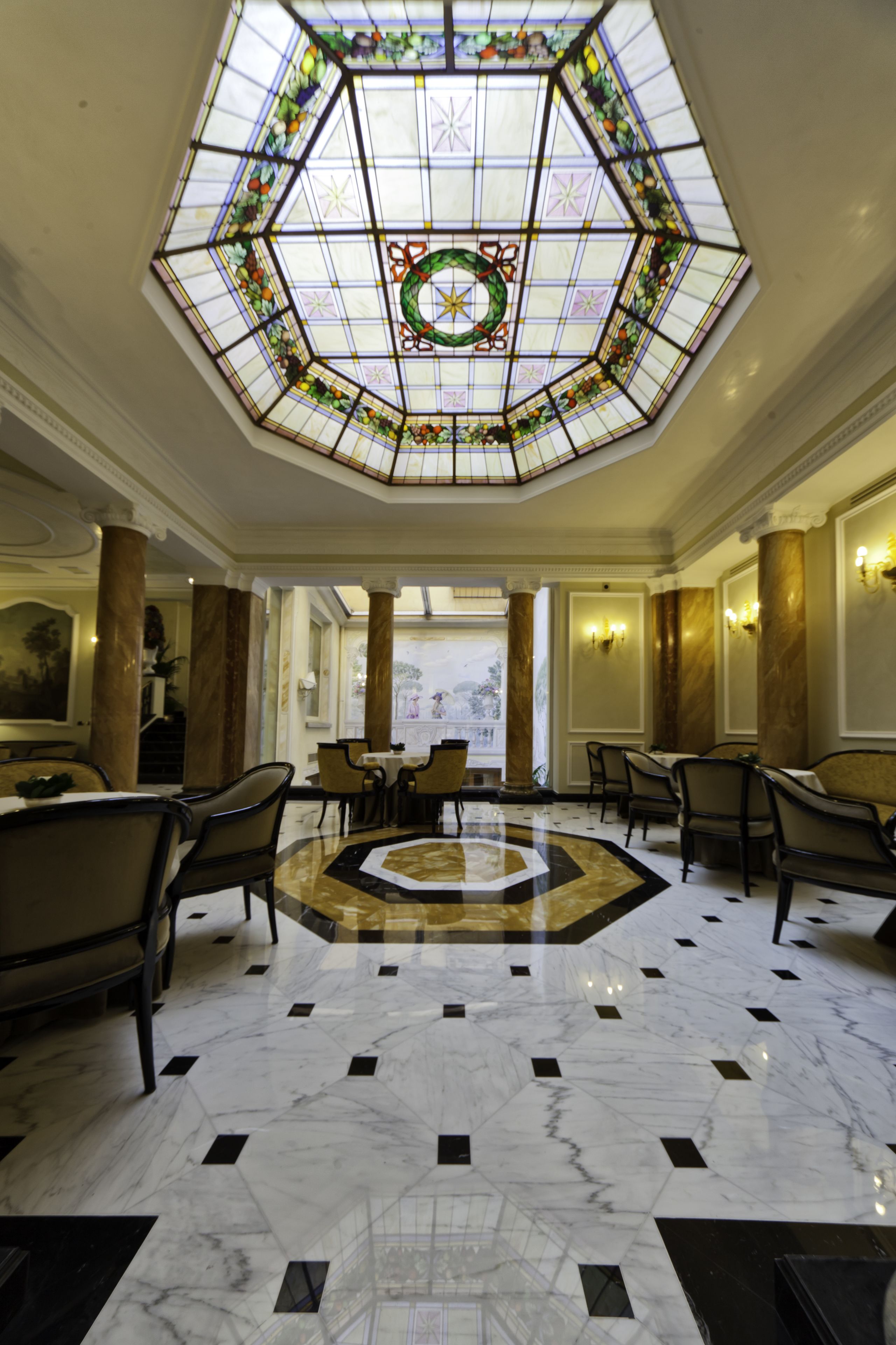 A lobby with a geometric patterned floor, a central chandelier, and a stained glass ceiling.