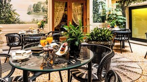 A dining area with round tables, wicker chairs, and potted plants.