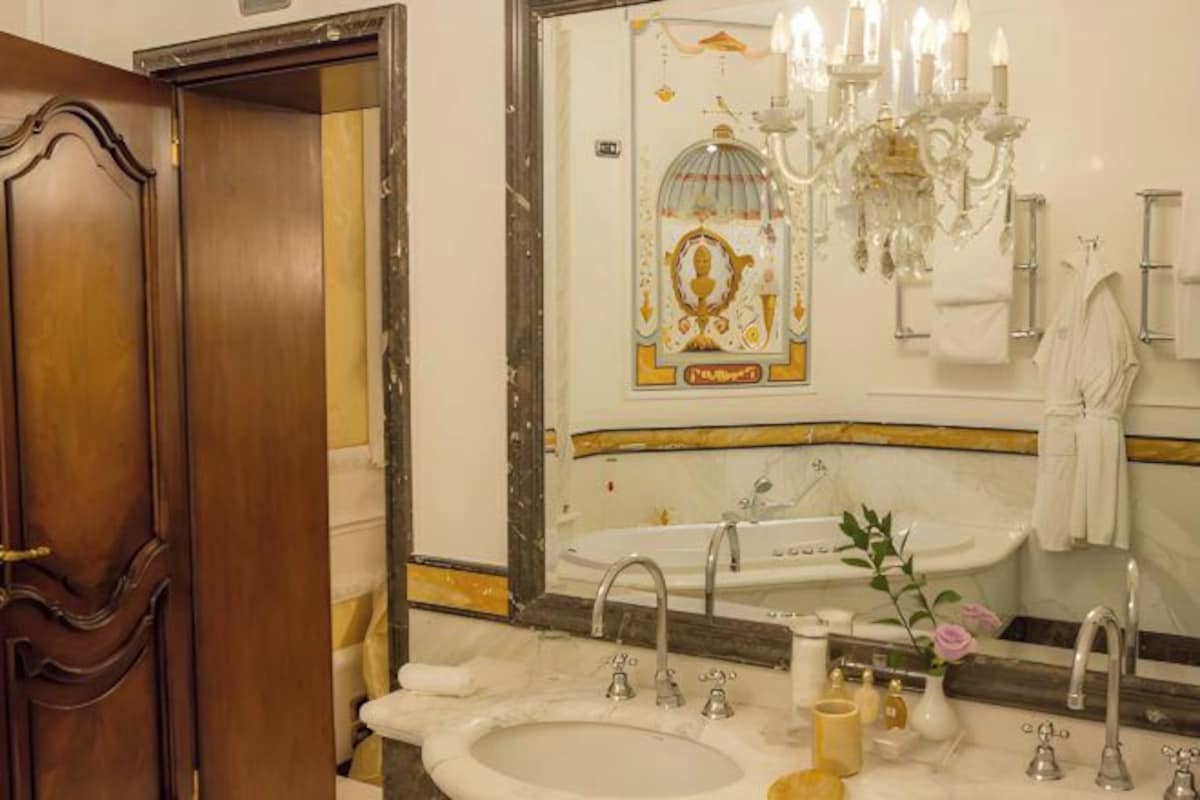 Un baño con un espejo grande, dos lavamanos, una araña y una puerta de madera.