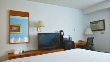 Habitación de hotel con cama, televisión, cafetera, escritorio con lámpara y espejo.