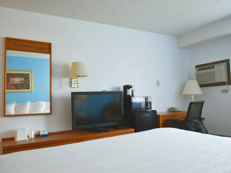 Habitación de hotel con cama, televisión, cafetera, escritorio con lámpara y espejo.