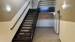 Una escalera con barandilla metálica, paredes color beige y suelo de baldosas.