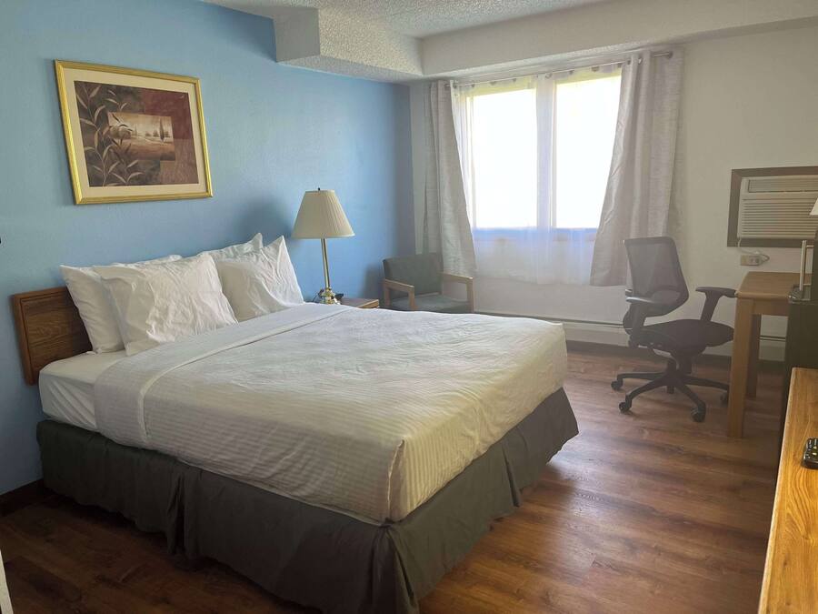 Een hotelkamer met een bed, bureau, stoel en raam met gordijnen.