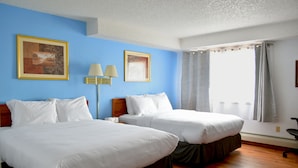 Una habitación de hotel con dos camas, una mesita de noche con lámparas y una ventana con cortinas.