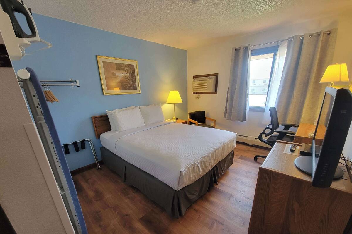 A hotel room with a bed, bedside lamps, a desk with a computer, and a window with curtains.