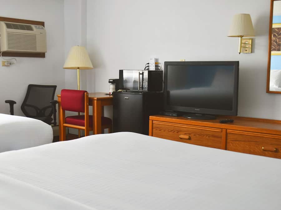 A hotel room with two beds, a desk with a television, a coffee machine, and a lamp.