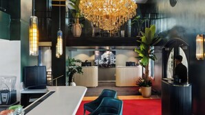 Een hotelhal met een kroonluchter, receptiebalie, zithoek en potplanten.