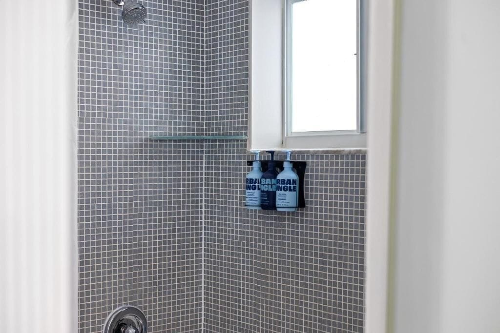 A bathroom with a shower, a window, and a shelf with bottles.
