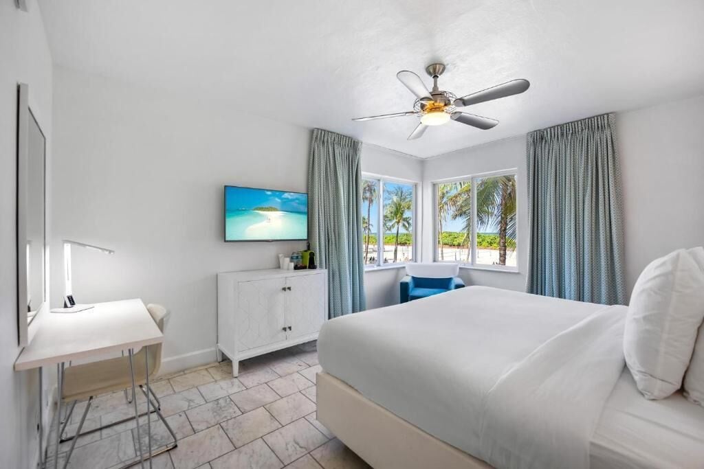 Ein Schlafzimmer mit Bett, Schreibtisch, Stuhl, Fernseher und Deckenventilator.
