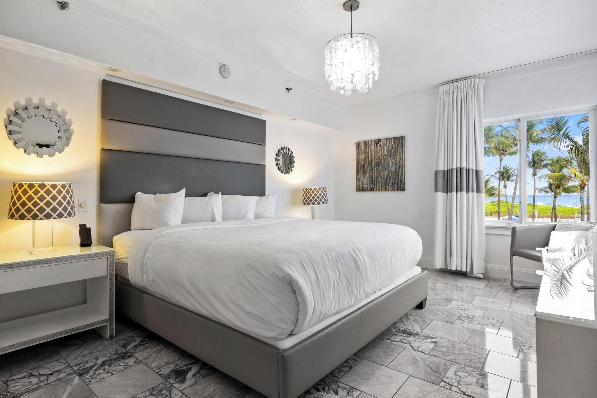 Un dormitorio moderno con una cama grande, suelo de mármol y vistas a palmeras a través de la ventana.