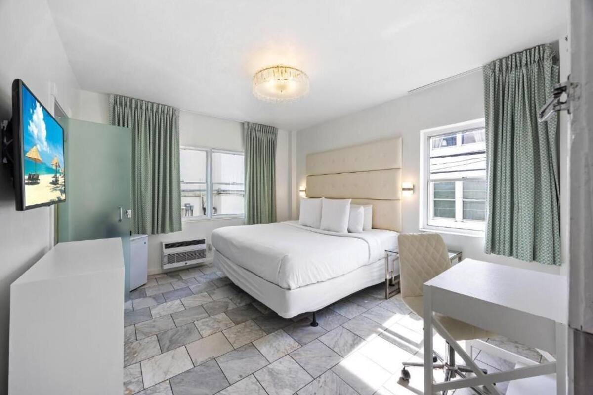 A hotel room with a bed, a desk, a chair, a TV, and a window with curtains.