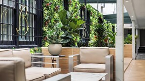 Een moderne zithoek met lederen banken en een marmeren tafel, omringd door weelderige groene planten en een zwarte metalen balustrade.