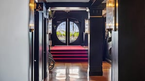 Een hotelingang met een rode loper die naar een dubbele deur met een rond raam leidt.