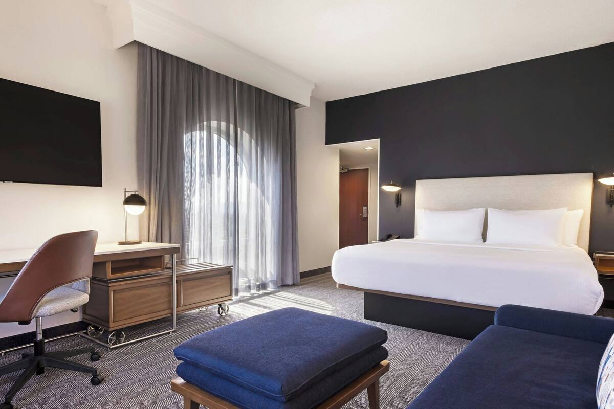 A hotel room with a bed, a desk, a chair, and a sofa.