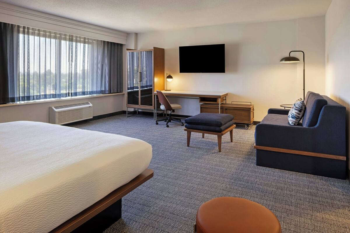 A hotel room with a large bed, a desk, a chair, a sofa, and a TV.
