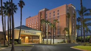 Un hotel Courtyard by Marriott con fachada moderna, palmeras y una entrada bien iluminada.