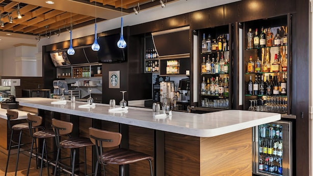 Zona de bar moderna con una barra alargada, varios taburetes y una gran variedad de botellas de licor.