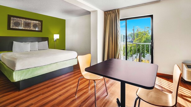 Quarto de hotel com cama, duas cadeiras, uma mesa, janela com vista e iluminação no teto.