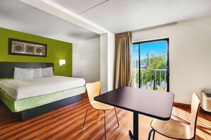 A hotel room with a bed, two chairs, a table, a window with a view, and a ceiling light. - Motel 6 Lawrenceville, NJ (Lawrenceville)