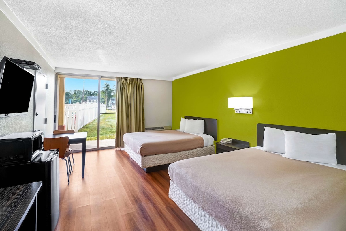 A hotel room with two beds, a desk, a TV, and a view of the outdoors.