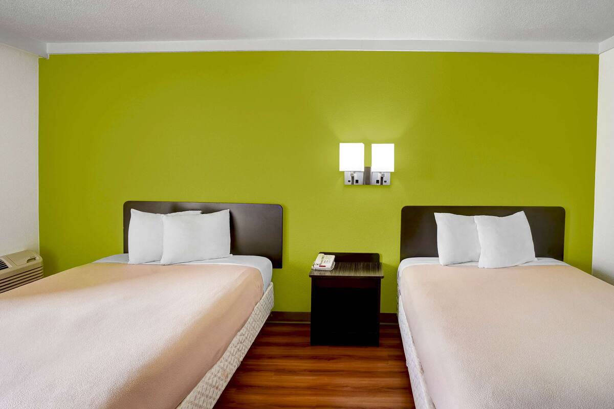 A hotel room with two beds, green walls, and a small bedside table with a phone.