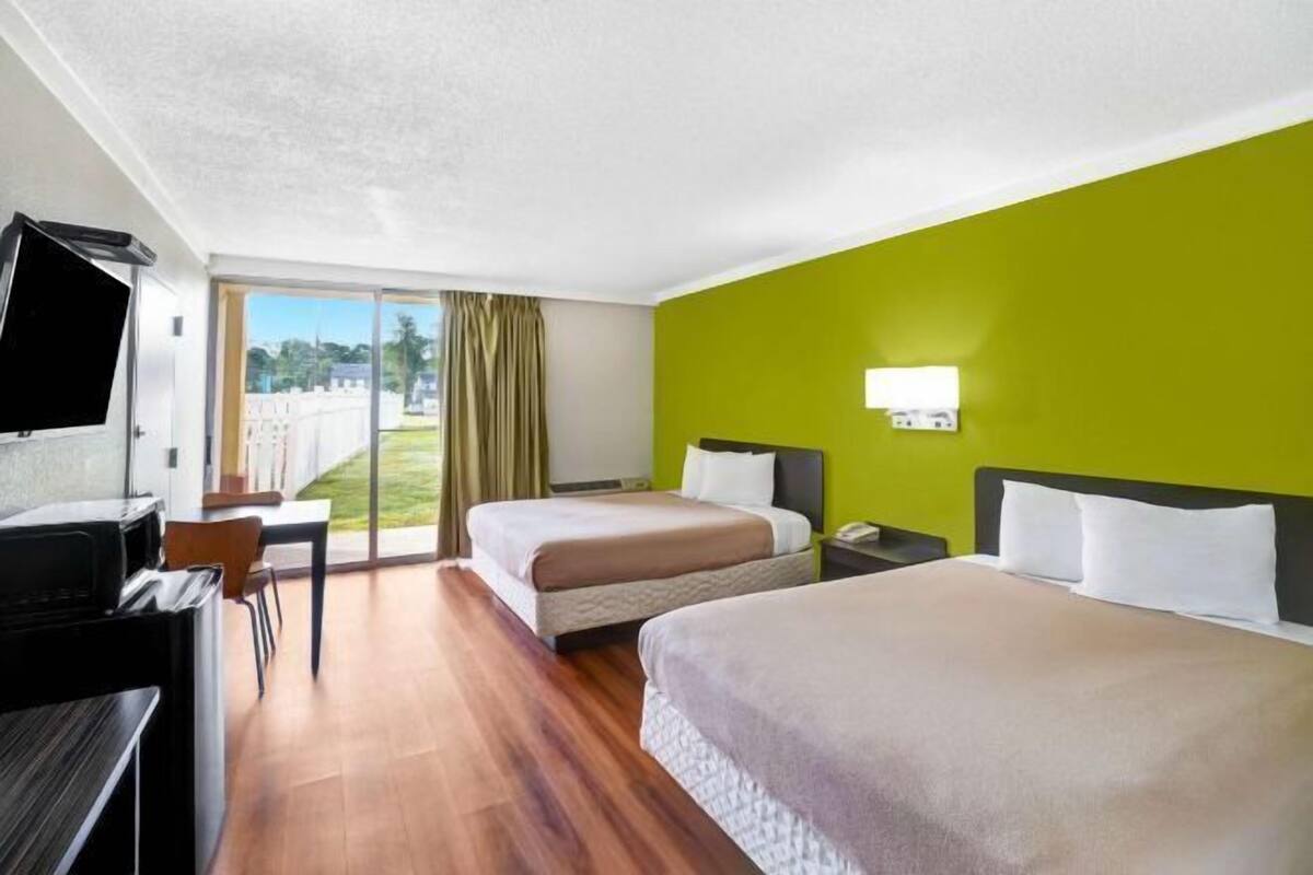 A hotel room with two beds, a desk, a TV, and a view of the outdoors.