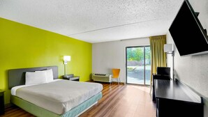 Quarto de hotel com cama, escrivaninha, cadeira, televisão e janela com vista para o exterior.